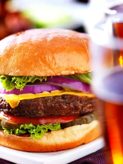 Delicious gourmet cheeseburger with fresh lettuce, tomato, onion, and melted cheese on a toasted bun, served with a cold beer.