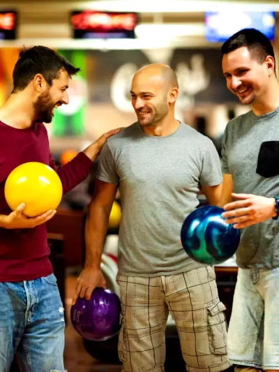 Group of friends laughing and holding bowling balls at Strikers Bowling, enjoying a fun night out.