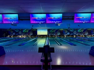Neon-Lit Bowling Lanes with Digital Scoreboards at Strikers A view of bowling lanes under neon lighting, featuring digital scoreboards and a modern bowling alley atmosphere.