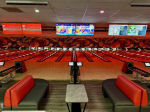 Strikers Bowling Alley – Red-Themed Lanes & Modern Seating Modern Best Bowling in Sunrise FL with red-themed lanes, digital scoreboards, and stylish seating area with black and red couches.