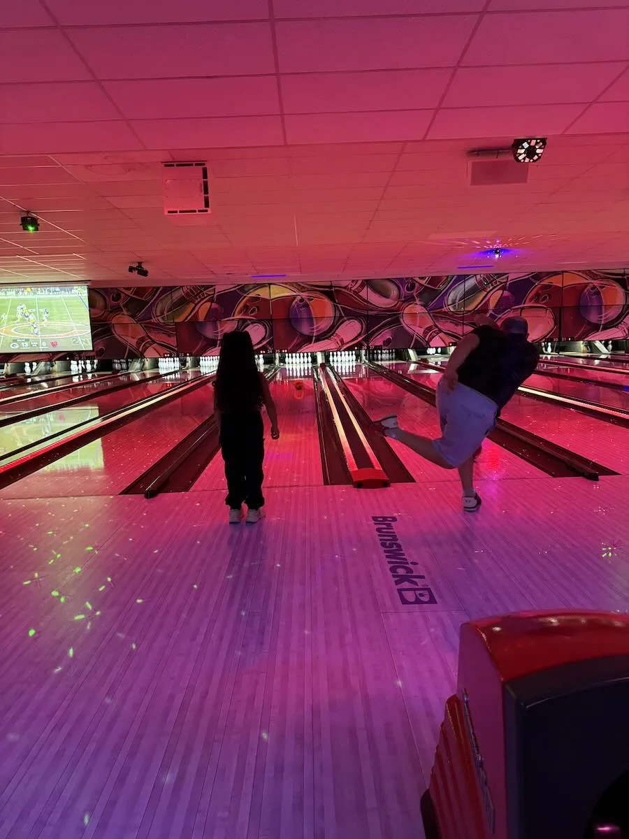 Family enjoying cosmic bowling at Strikers Sunrise as a bowler releases a shot on illuminated lanes under colorful LED lighting in Sunrise, Florida.