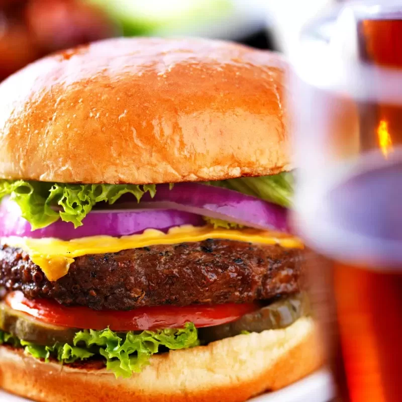 Delicious gourmet cheeseburger with fresh lettuce, tomato, onion, and melted cheese on a toasted bun, served with a cold beer.